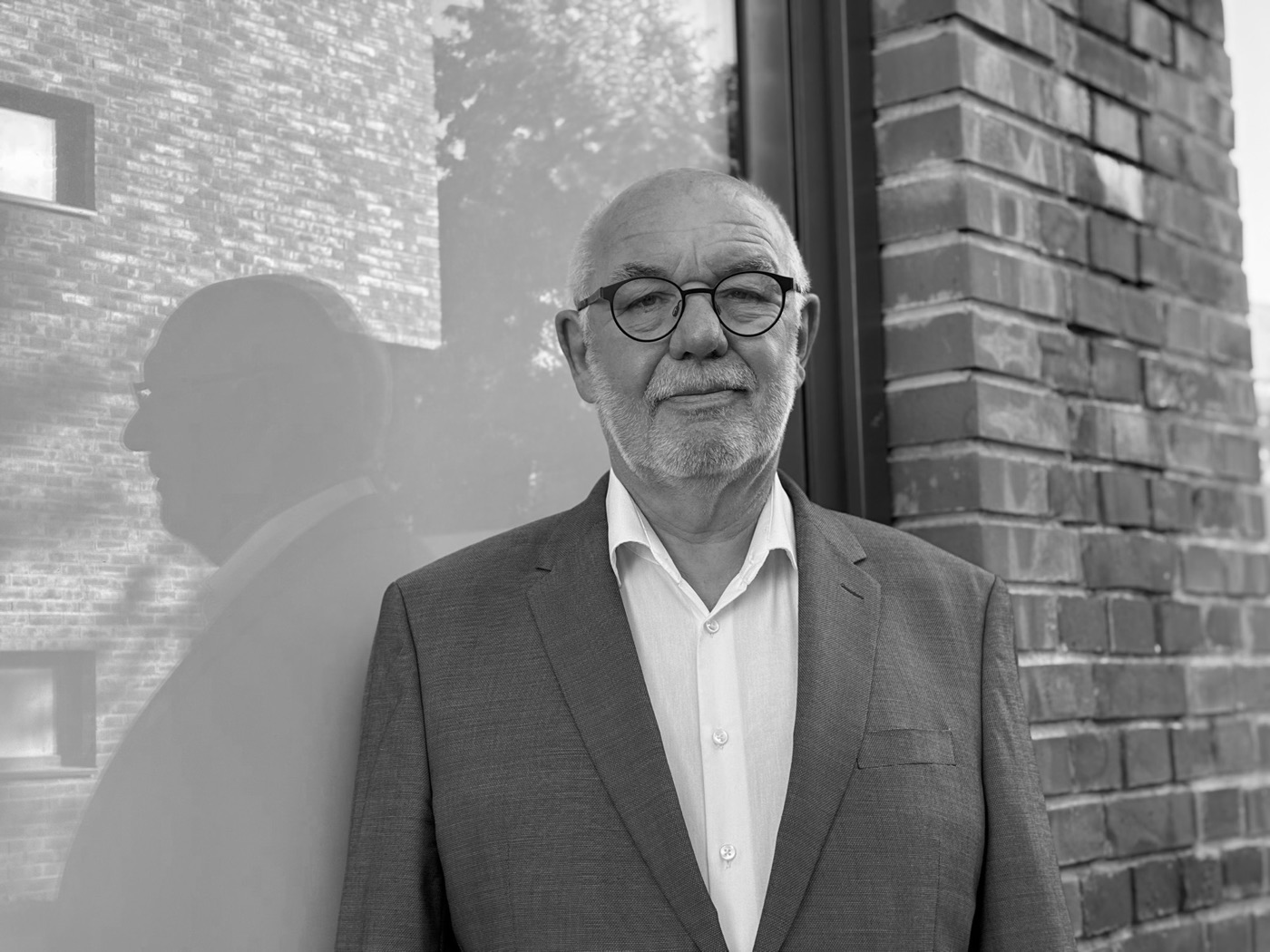 Detlef Durdel in Sakko und weißem Hemd vor einer Klinkerwand, Schwarzweißporträt